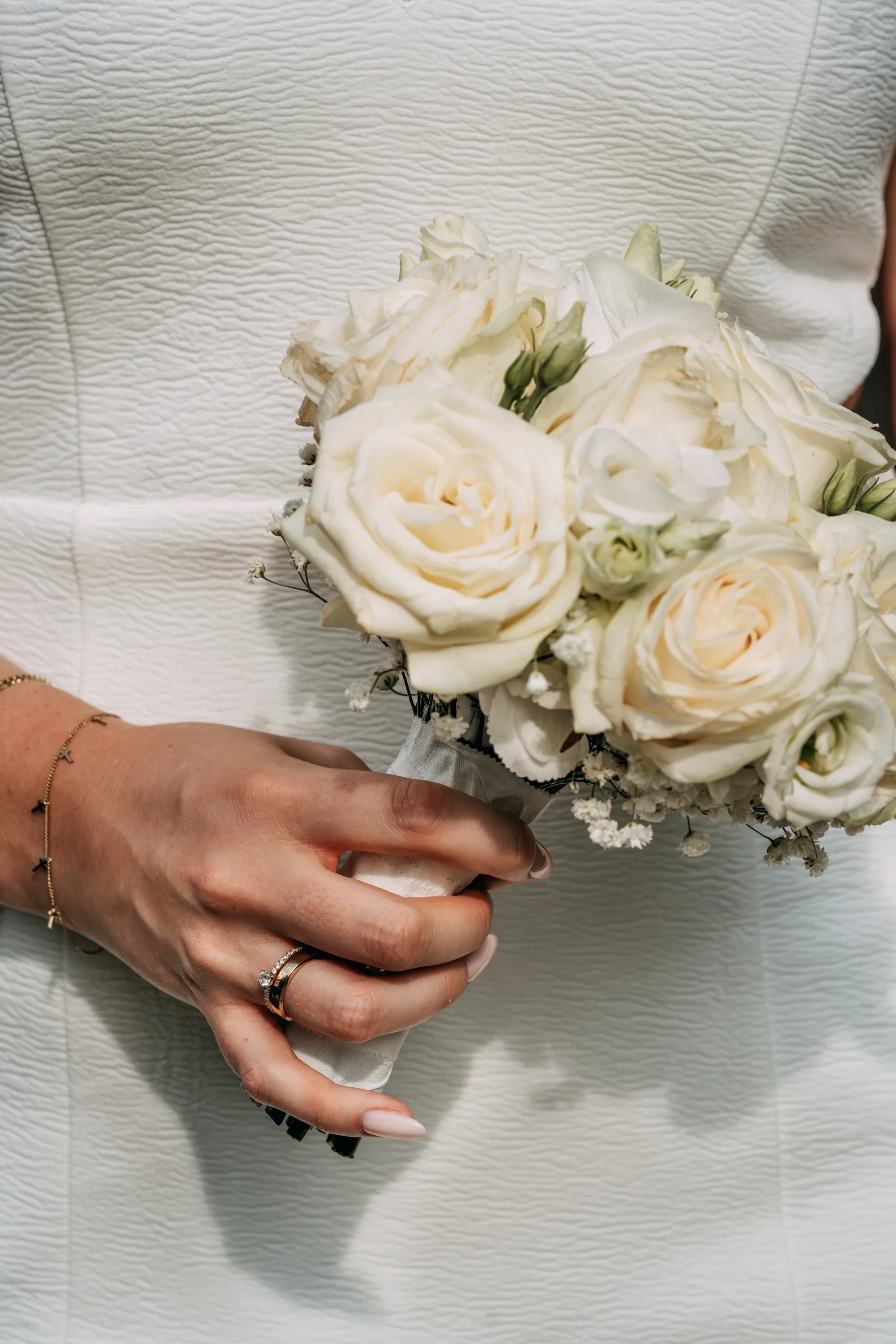 Braut hält einen weißen Rosenstrauß vor ihrem Kleid, Nahaufnahme der Hand mit Ring