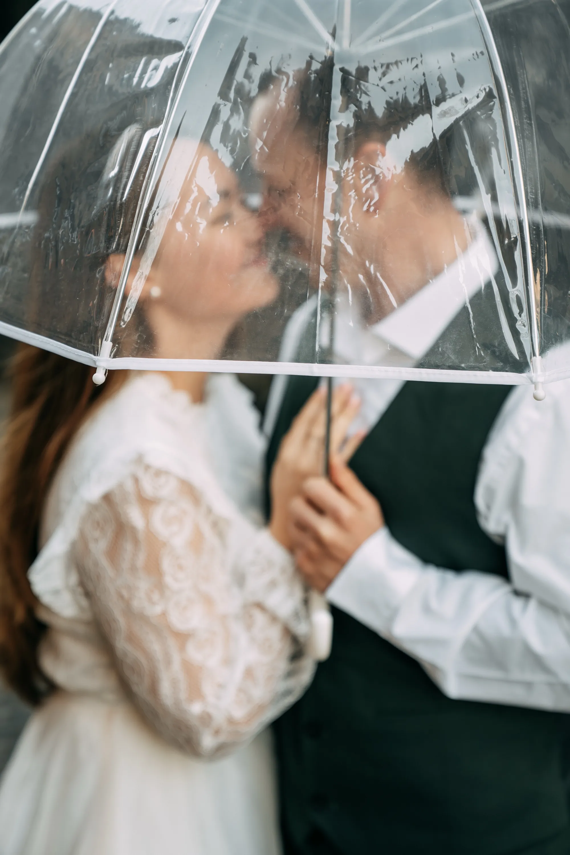 Brautpaar küsst sich unter einem durchsichtigen Regenschirm im Regen